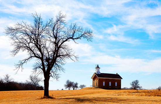 A rural Kansas church stands behind an autumn tree.